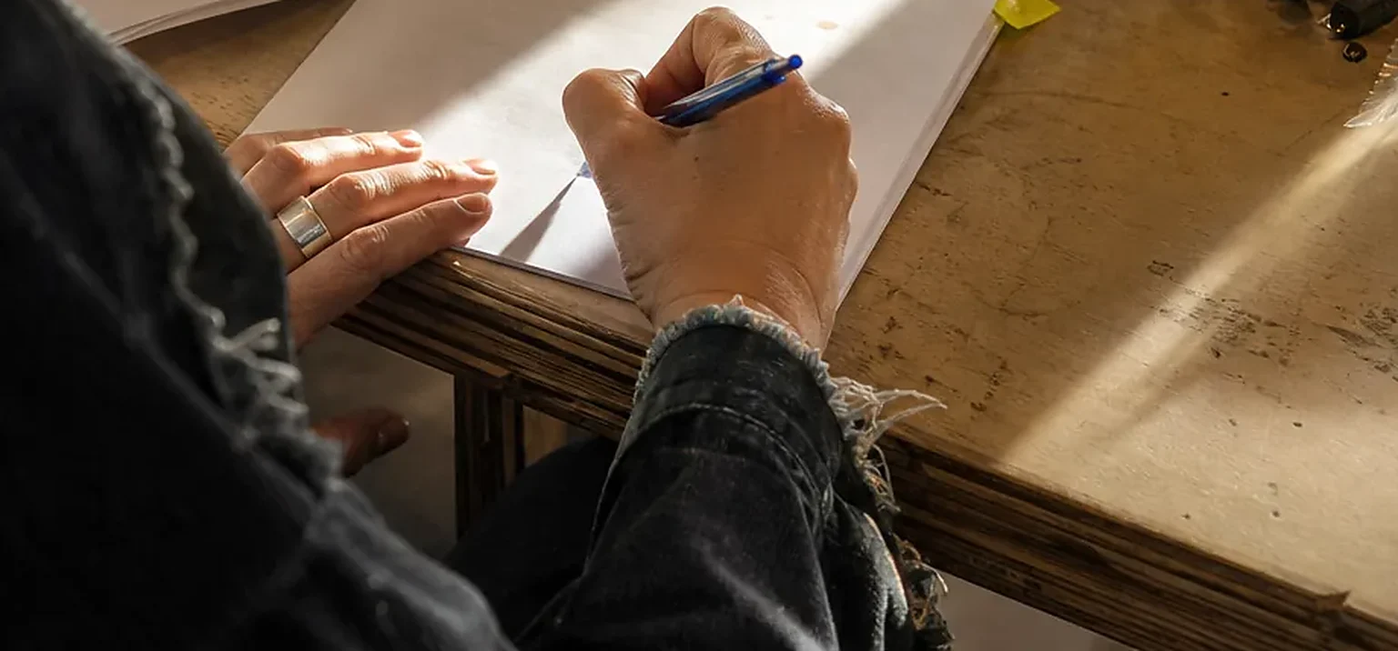 Hands signing a printed agreement with a blue pen on a wooden desk